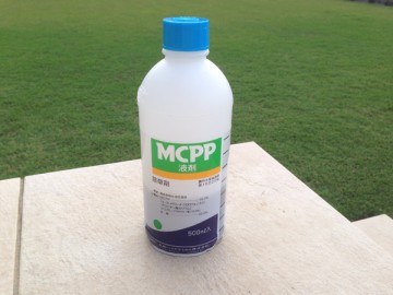 A bottle of herbicide, MCPP. In front of tile deck and green lawn.