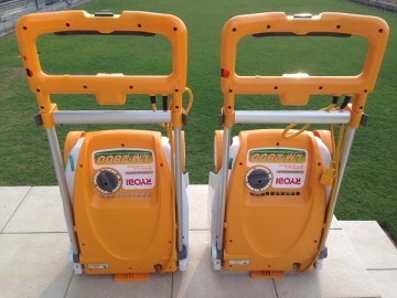 Two yellow Ryobi lawn mowers. In front of the tile deck and green lawn.