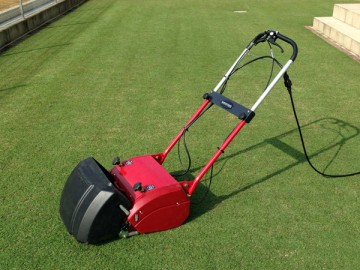 A close up of the red mowing machine, in front of the green lawn after mowing.
