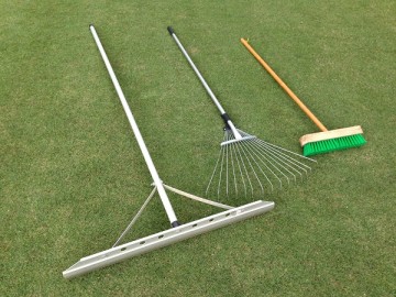 An aluminum rake, an aluminum lawn rake, and a deck brush arranged on the green lawn.