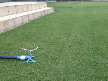 Four aligned blue sprinkler on green lawn. A view from the other side.