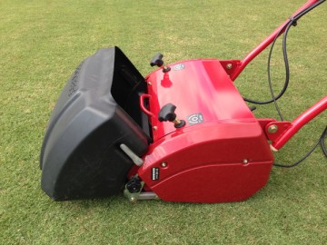 A black resin-made grass collector box attached to the red mowing machine.