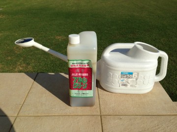 A 2L bottle of ALM Green and a 6 L watering pot in front of the lawn.