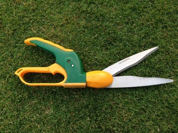 An angle adjustable grass shear in yellow and green, placed on the green lawn.