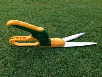 An angle adjustable grass shear on the lawn. The handles are vertical to the shears.