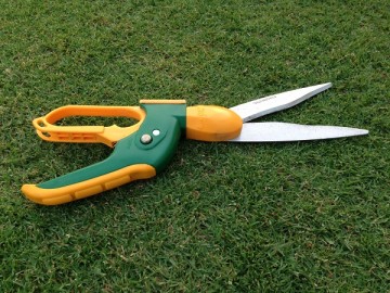 An angle adjustable grass shear on the lawn. The handles are horizontal to the shears.