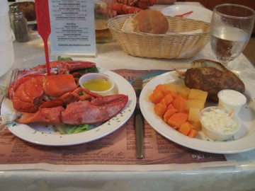 A whole lobster, potatoes, vegetables, and breads on the table.