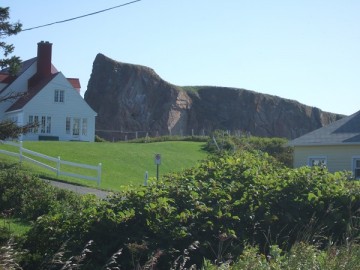 Lawn, several white houses with red roofs, and a massive rock behind them.