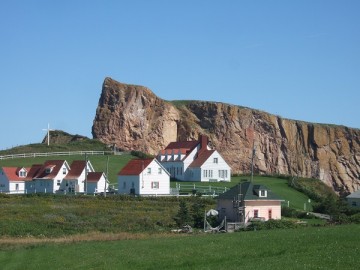 Several white houses with red roofs in the lawn, and a massive rock behind them.