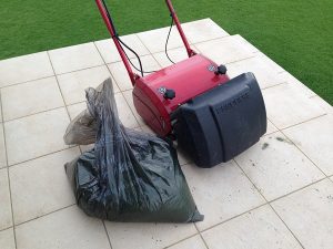 芝刈り後の赤い芝刈り機LM12MHと、刈り芝の入った黒いゴミ袋。